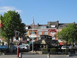 Camion de vidange devant l'église Saint-Pierre à Bastogne éclairée par le soleil, architecture typique et rues pavées.