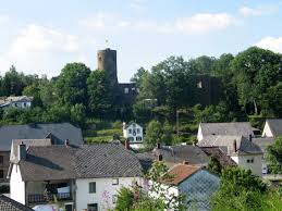 Vidange Burg-Reuland camion devant l'église typique du village entouré de maisons traditionnelles et de verdure.
