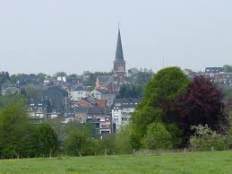 Scène urbaine à Kelmis avec un garage local pour vidange, rues pavées et bâtiments historiques typiques de la région.