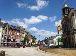 Vue sur la place Saint-Michel à Neufchâteau avec un camion de débouchage prêt à intervenir, scène animée en centre-ville.