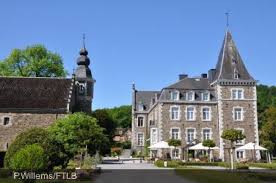 Camion de vidange sur une rue bordée d'arbres à Rendeux près d'un bâtiment en pierre typique des Ardennes.