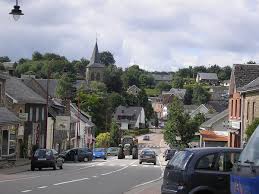 Camion de vidange dans une rue pittoresque de Waimes avec maisons en pierre et verdure environnante