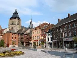 Scène urbaine à Soignies avec une entreprise de vidange locale au cœur de la ville historique, proche des rues pavées et de l'église.